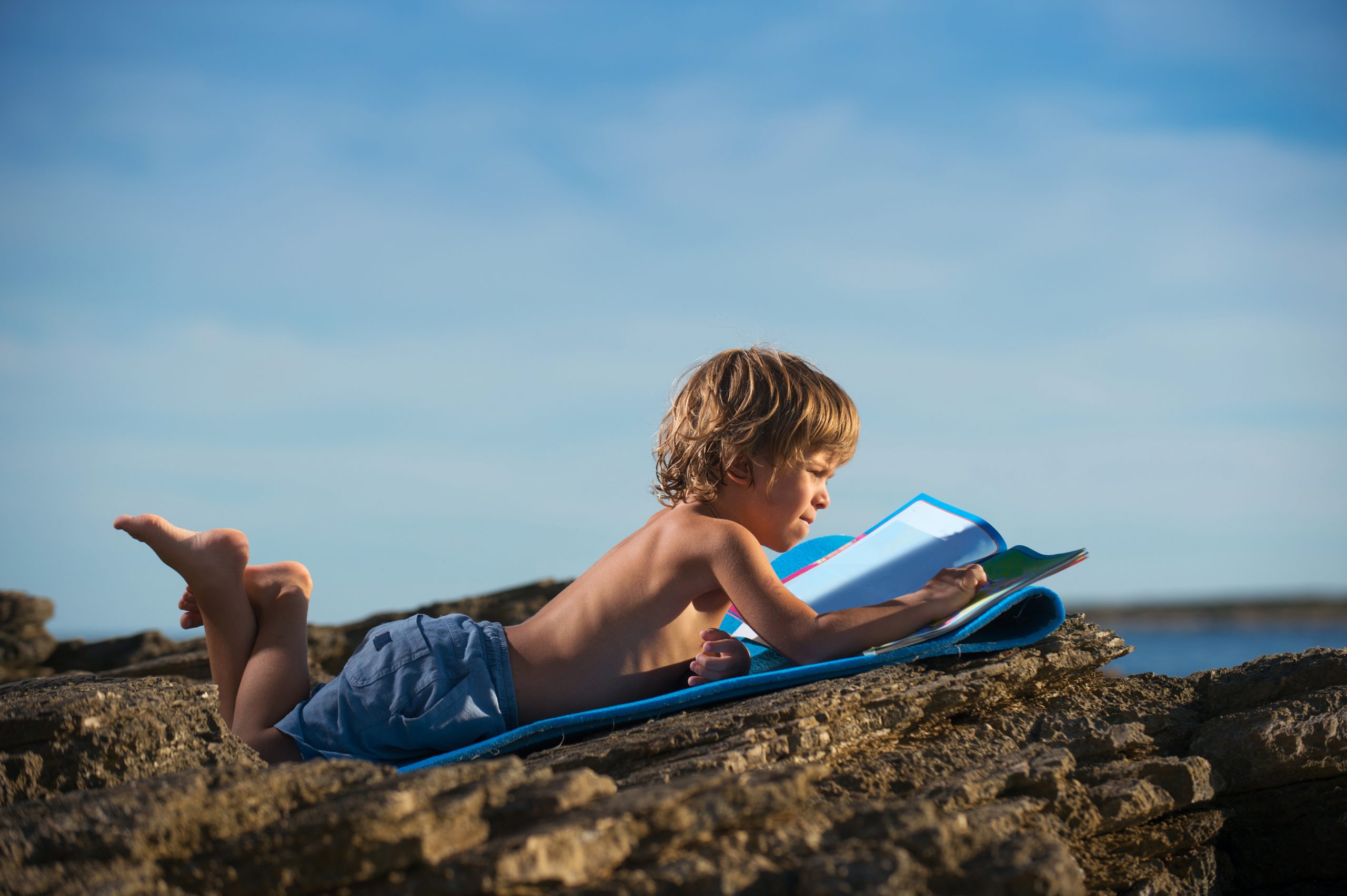enfant sur la plage avec son cahier de vacances